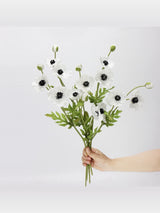 White artificial poppy stems held in hand to show the flower arrangement