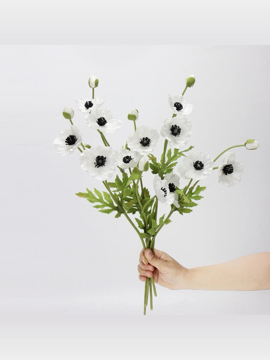 White artificial poppy stems held in hand to show the flower arrangement