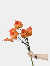 Hand-held orange faux anthurium stems showing their scale and colour