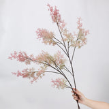 Pink faux asparagus fern branch held for scale
