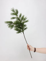 One green faux pine branch held by hand