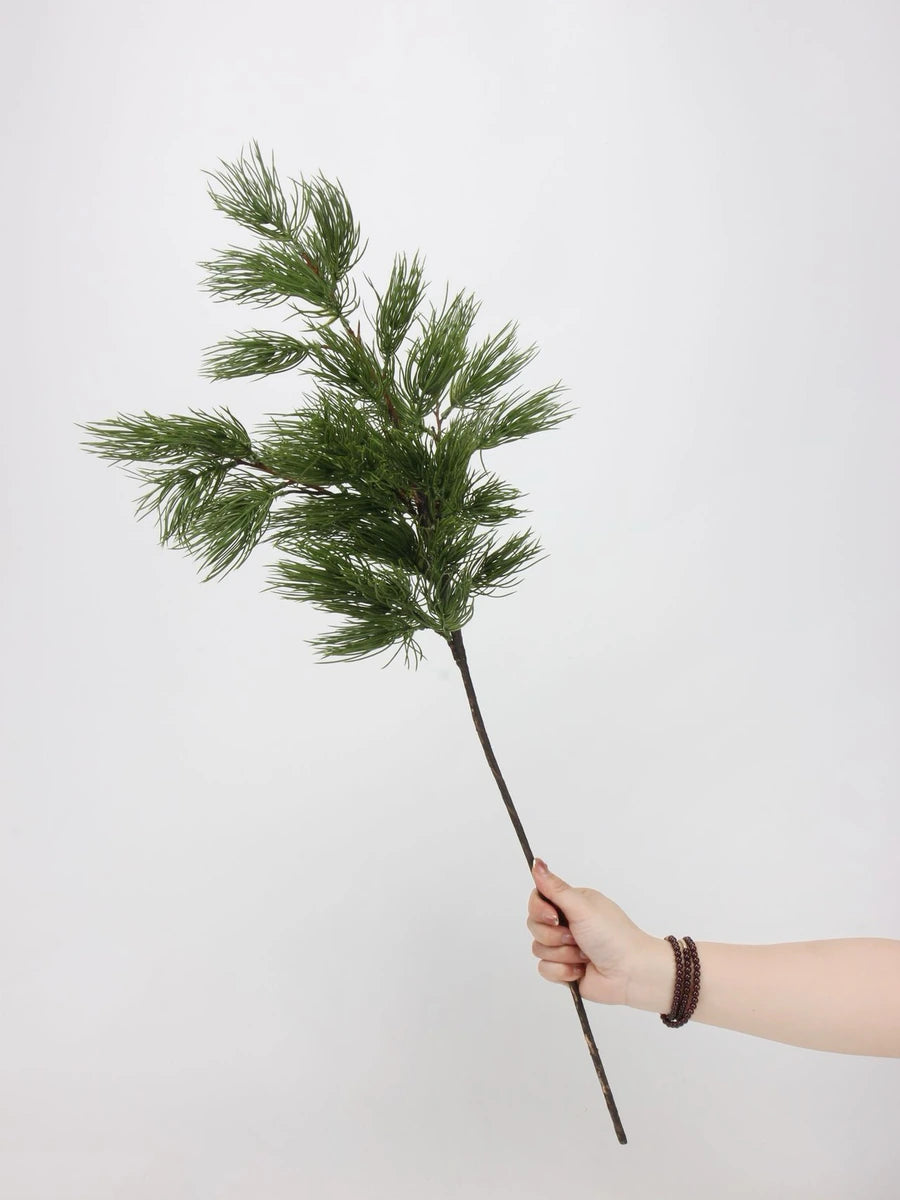 One green faux pine branch held by hand