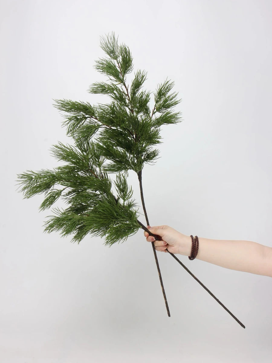 Two green faux pine branches held by hand