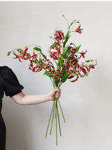 Red artificial gloriosa lily stems held as a bouquet