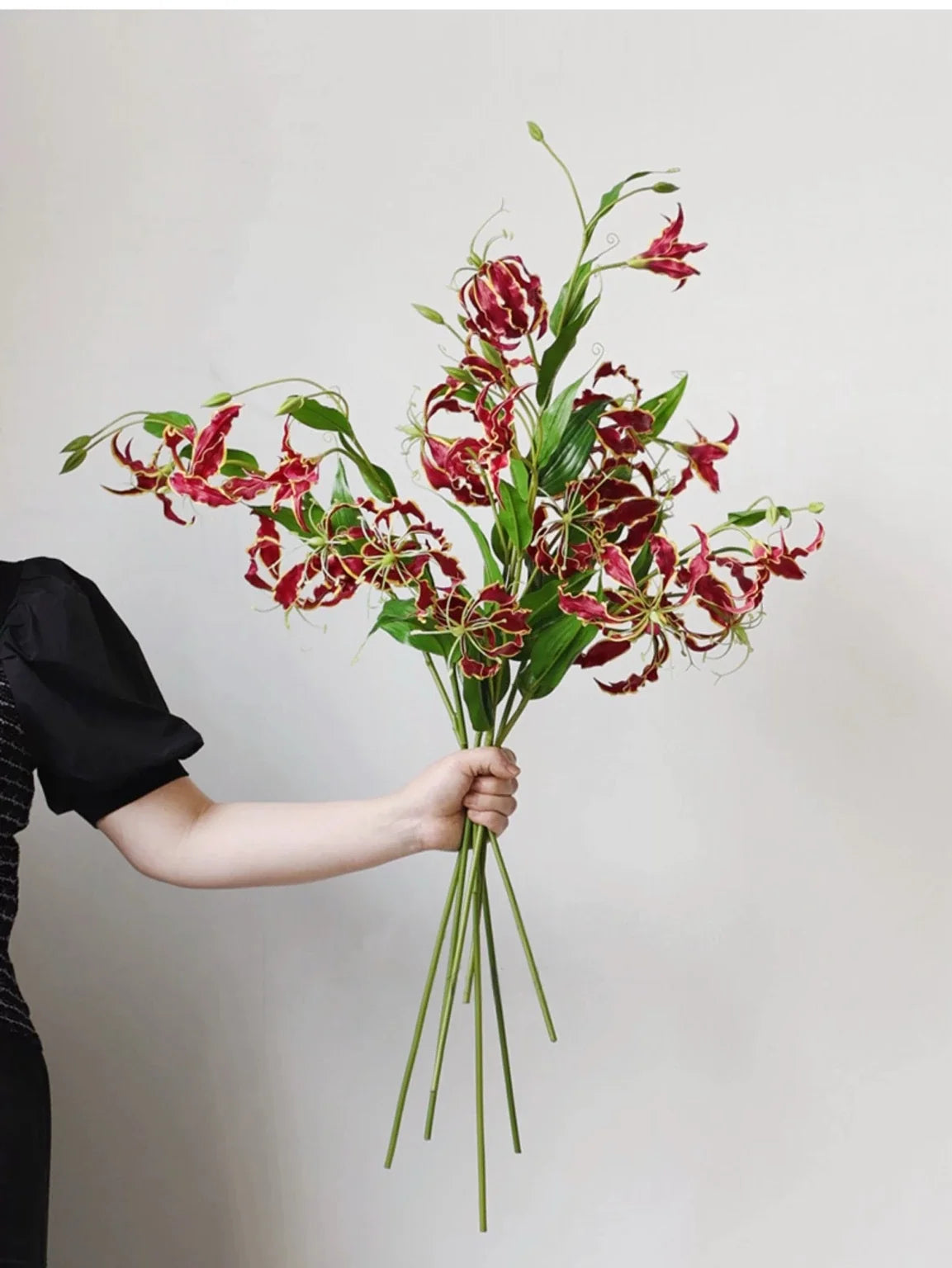 Red artificial gloriosa lily stems held as a bouquet
