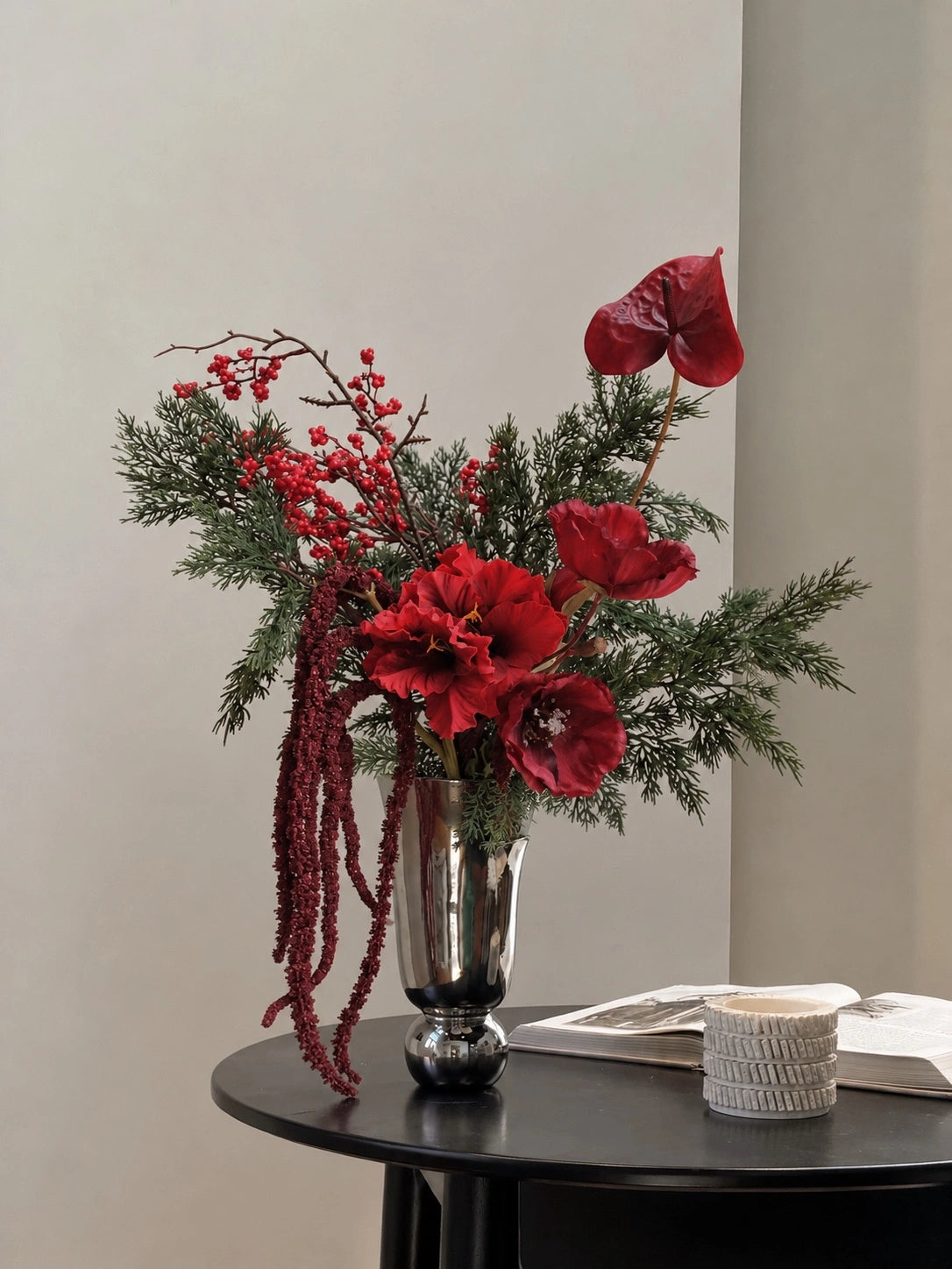 Noël faux Christmas bouquet with red blooms, berries, burgundy trailing foliage and evergreen branches; vase shown for styling