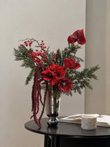 Noël faux Christmas bouquet with red blooms, berries, burgundy trailing foliage and evergreen branches; vase shown for styling