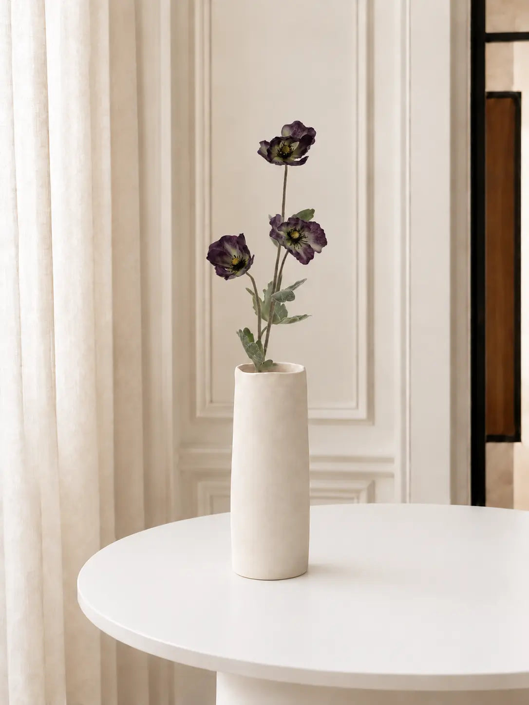 One dark purple faux Siberian anemone stem in an ivory vase, with soft diffuse light; vase not included.