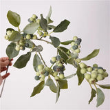 Green faux berry branch held by hand, close-up