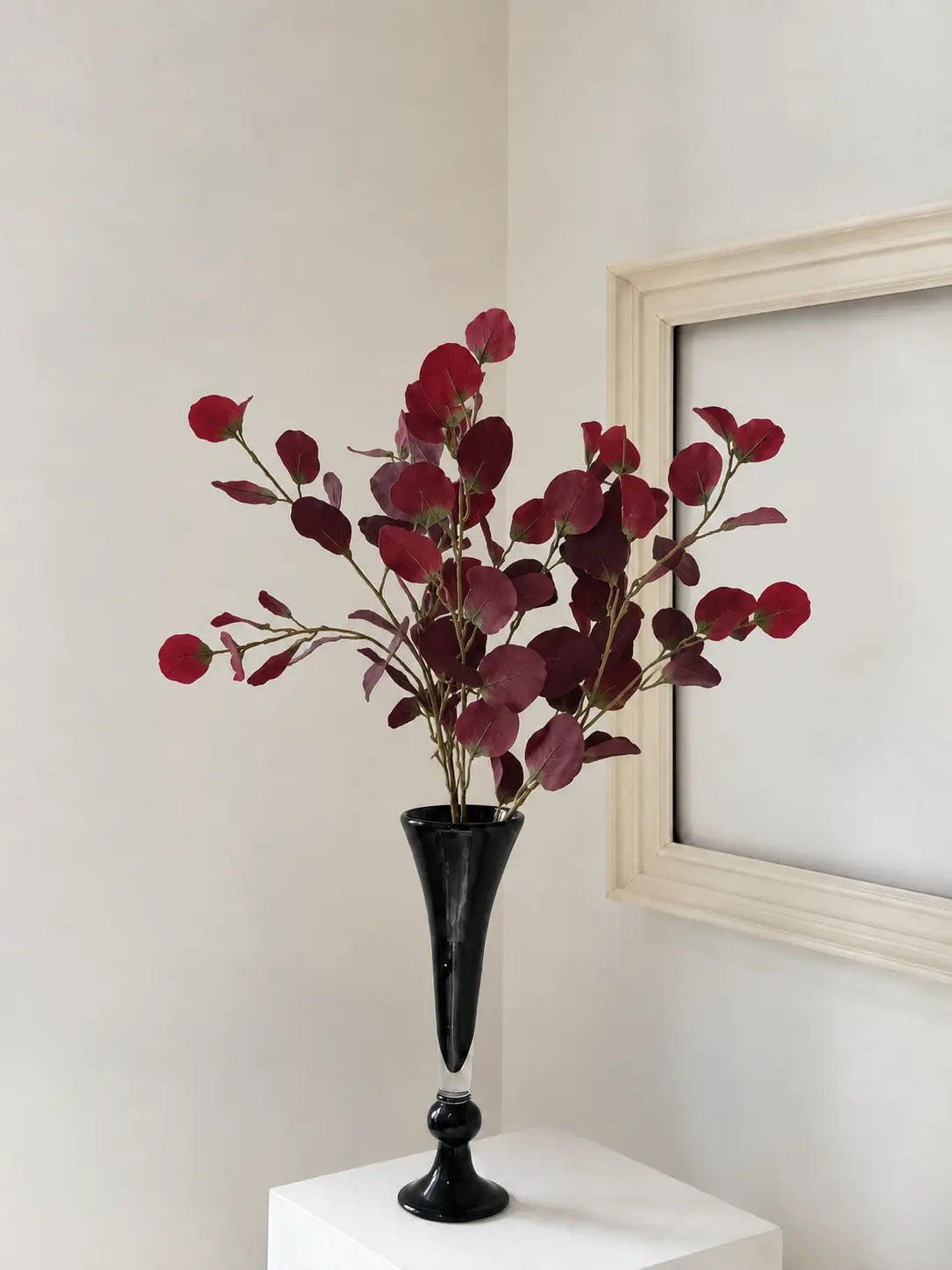 Three burgundy faux vintage eucalyptus stems arranged naturally in a tall black vase