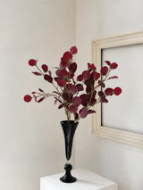 Three burgundy faux vintage eucalyptus stems arranged naturally in a tall black vase